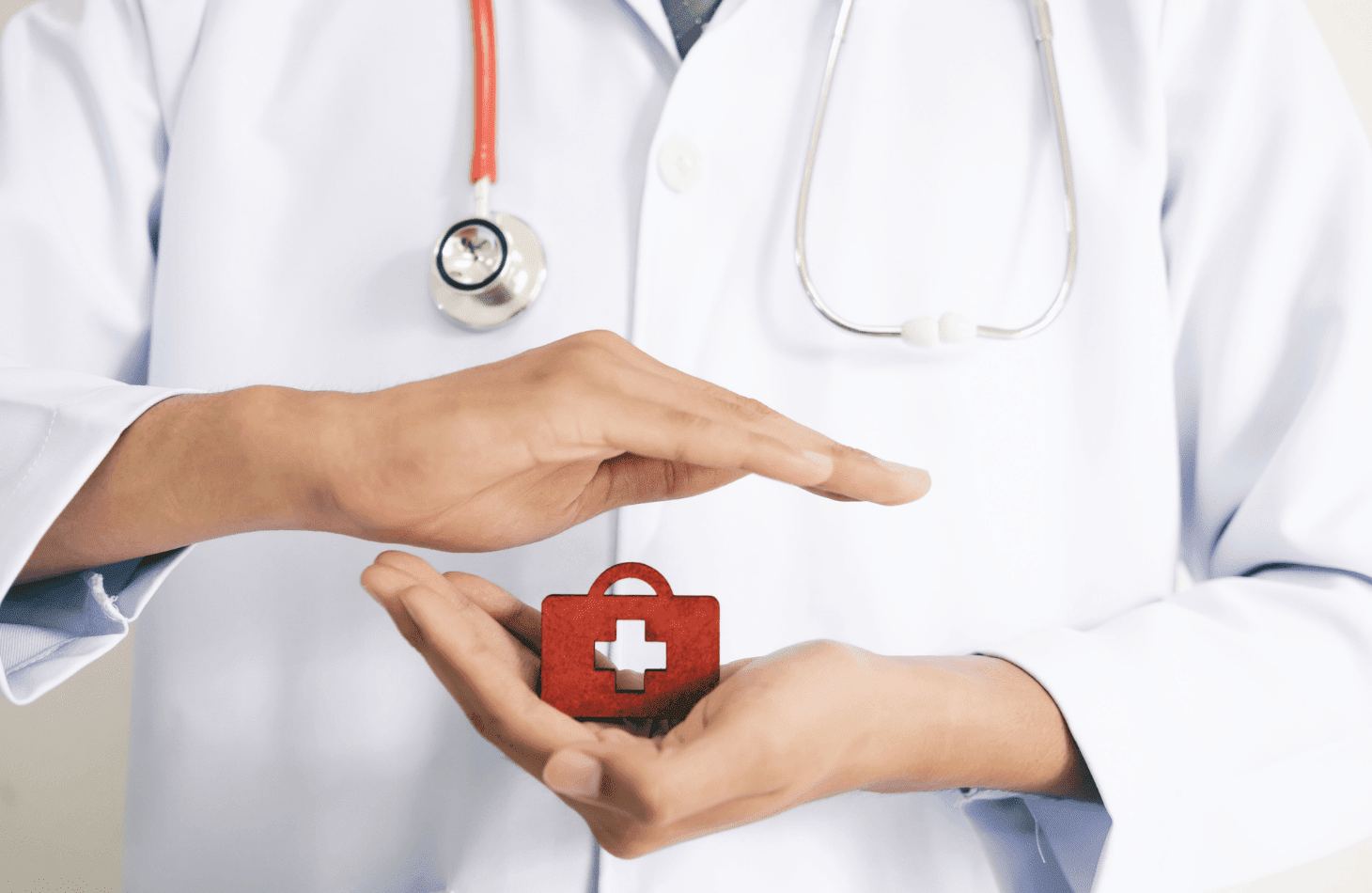 Une personne en blouse blanche tient entre ses mains une mini mallette rouge qui représente la santé au travail